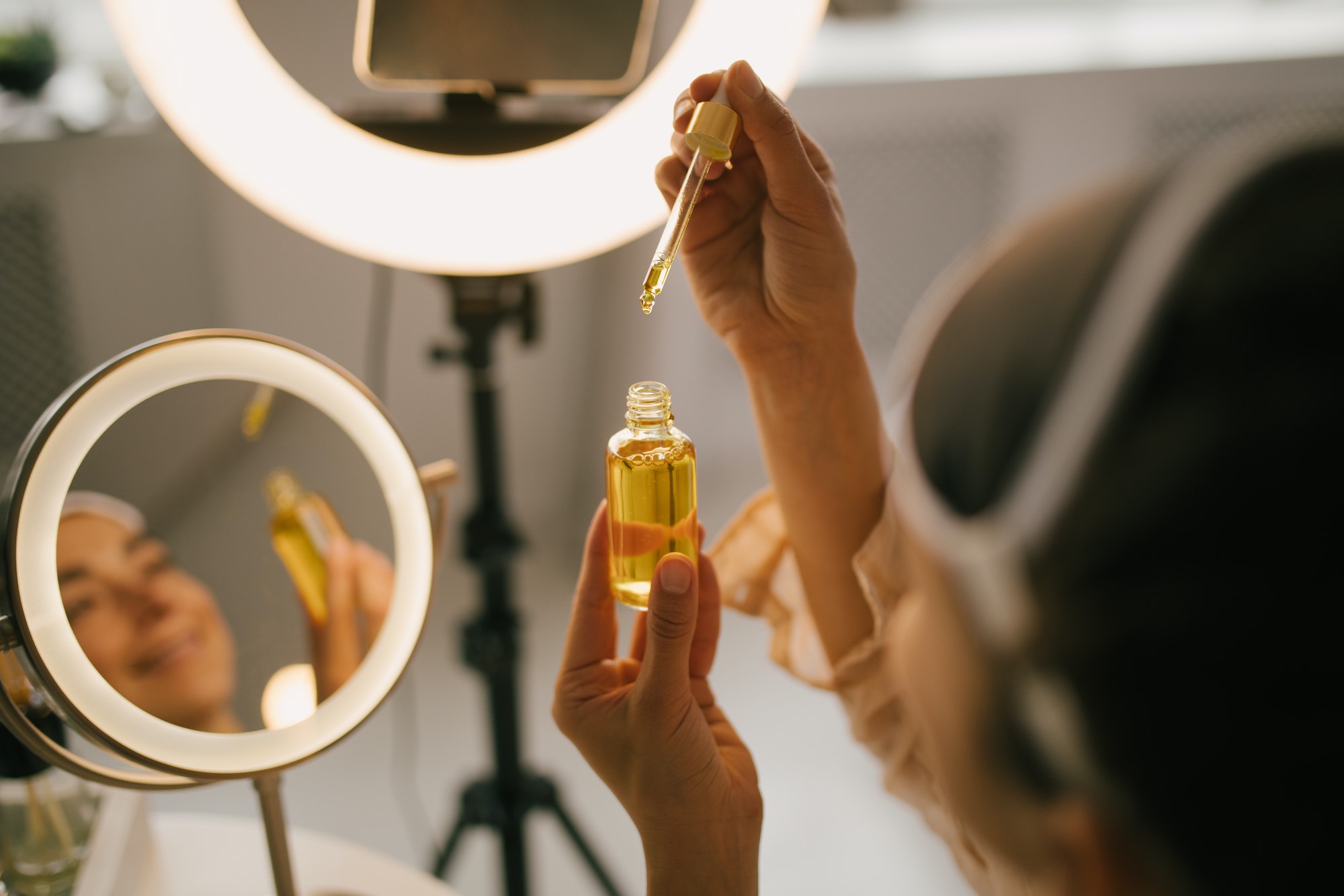 Woman holding natural face oil close up. Blogger recording video demonstration of beauty products.